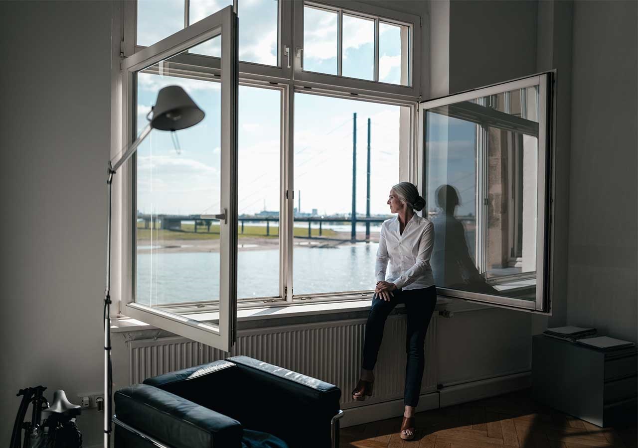 Frau sitzt am Fenster und blickt auf den Rhein. © Westend61 / Westend61 via Getty Images 